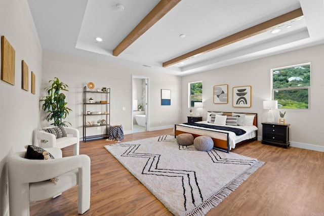 bedroom with connected bathroom, a raised ceiling, and light wood-type flooring