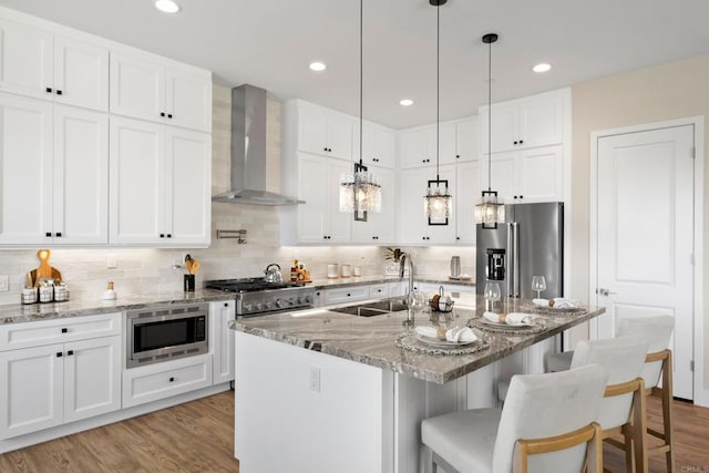 kitchen with appliances with stainless steel finishes, sink, white cabinetry, and wall chimney range hood