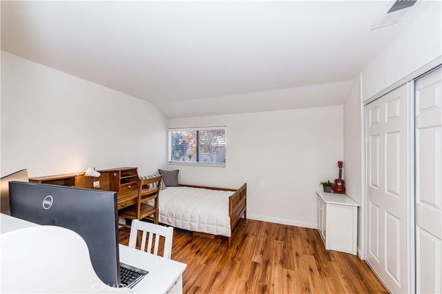 bedroom with lofted ceiling, light hardwood / wood-style flooring, and a closet