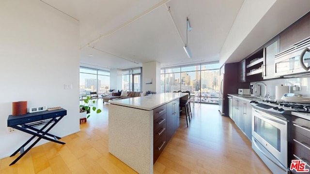 kitchen with dark brown cabinetry, appliances with stainless steel finishes, a center island, light wood-type flooring, and floor to ceiling windows