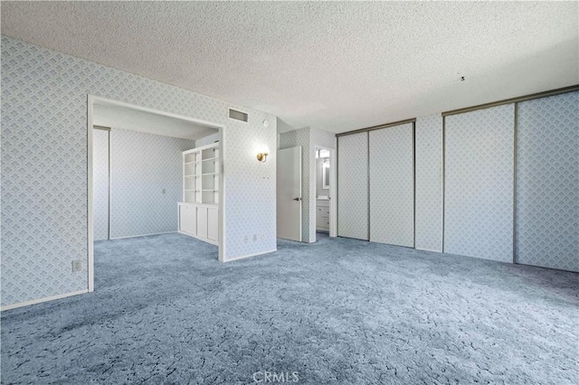 unfurnished bedroom featuring a textured ceiling, carpet flooring, and two closets