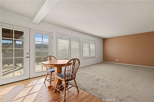 dining area featuring light colored carpet, french doors, beamed ceiling, and a textured ceiling