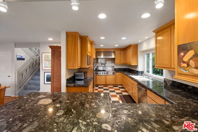 kitchen with sink, dark stone counters, wall chimney range hood, and stainless steel appliances