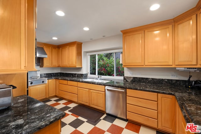 kitchen with stainless steel appliances, wall chimney range hood, dark stone counters, and sink