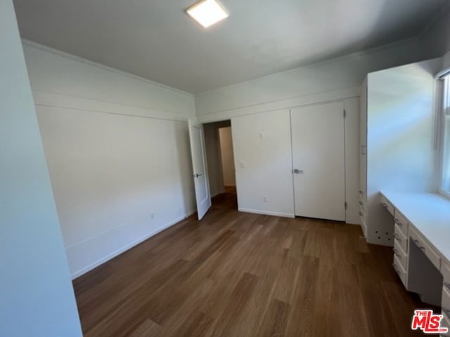 unfurnished bedroom with a closet, built in desk, and dark hardwood / wood-style floors