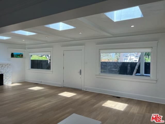 unfurnished living room featuring a skylight, a fireplace, hardwood / wood-style flooring, and beamed ceiling