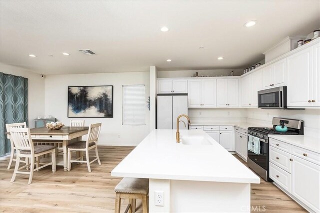 kitchen with a kitchen island with sink, stainless steel gas stove, white refrigerator, white cabinets, and sink