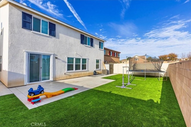 back of property featuring a lawn, a trampoline, and a patio area