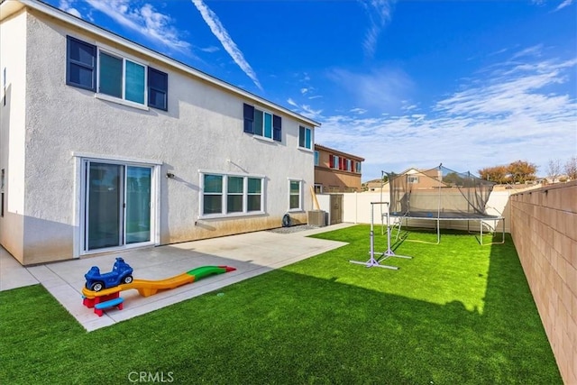 rear view of house with stucco siding, a trampoline, a fenced backyard, a yard, and a patio area