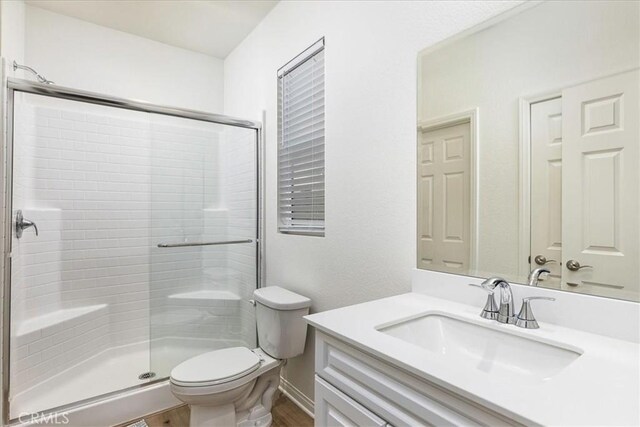 bathroom with wood-type flooring, toilet, a shower with door, and vanity