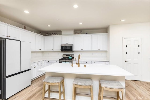 kitchen with appliances with stainless steel finishes, white cabinetry, and an island with sink