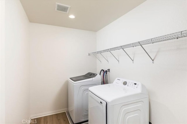 clothes washing area with visible vents, wood finished floors, separate washer and dryer, baseboards, and laundry area