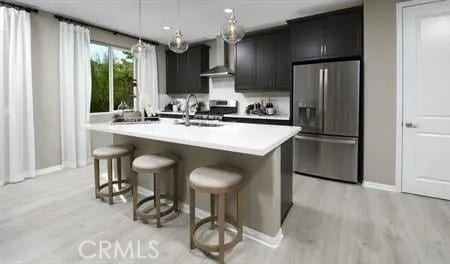 kitchen featuring pendant lighting, a breakfast bar, an island with sink, stainless steel appliances, and wall chimney exhaust hood