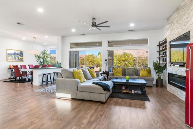 living room with ceiling fan, wood-type flooring, and a stone fireplace