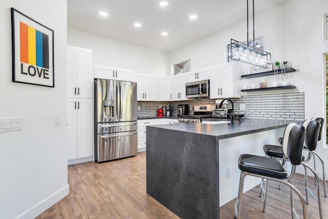 kitchen featuring kitchen peninsula, stainless steel appliances, pendant lighting, white cabinets, and a breakfast bar