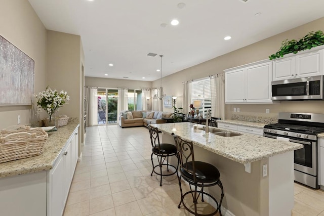 kitchen featuring light stone countertops, appliances with stainless steel finishes, white cabinetry, an island with sink, and sink