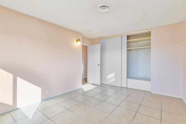 unfurnished bedroom featuring a textured ceiling, a closet, and light tile patterned flooring