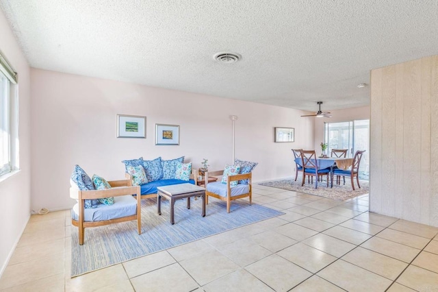 living area with ceiling fan, a textured ceiling, and light tile patterned floors