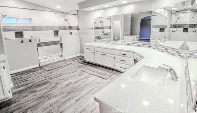 bathroom with double vanity, vaulted ceiling, a stall shower, wood finished floors, and a sink