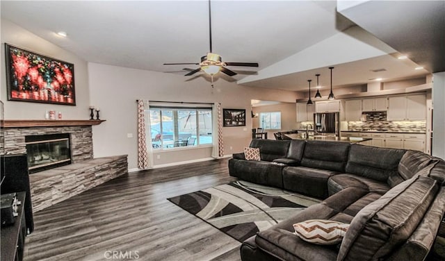 living room with baseboards, a fireplace, ceiling fan, vaulted ceiling, and dark wood-type flooring