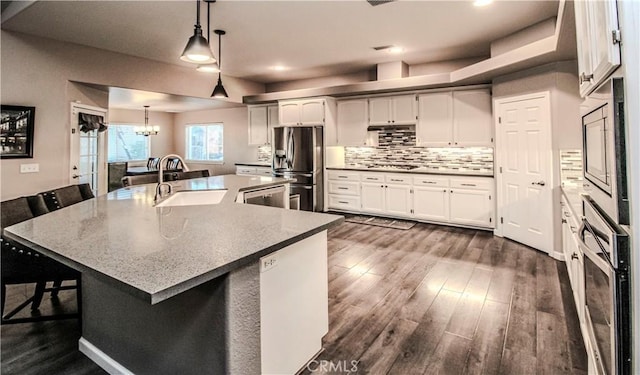 kitchen featuring a sink, dark wood-style floors, stainless steel appliances, a breakfast bar area, and decorative backsplash