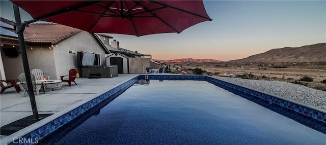 pool at dusk featuring a patio area, an outdoor pool, a mountain view, and a fire pit