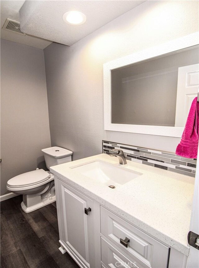 bathroom featuring vanity, wood finished floors, visible vents, toilet, and backsplash