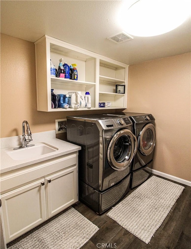 laundry area featuring visible vents, dark wood finished floors, cabinet space, a sink, and independent washer and dryer