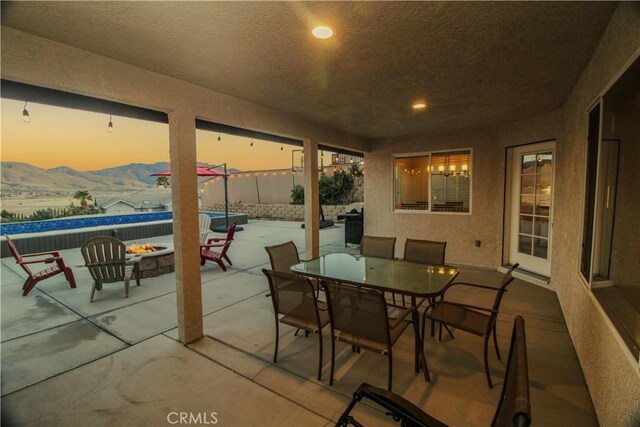 view of patio with a fire pit, fence, a mountain view, outdoor dining area, and an outdoor pool