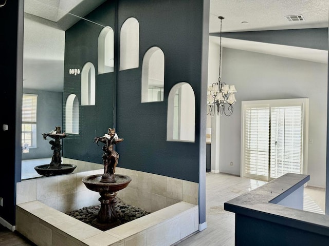 interior space with hardwood / wood-style flooring, a textured ceiling, a notable chandelier, and vaulted ceiling