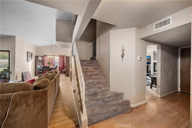 staircase with a textured ceiling, a chandelier, vaulted ceiling, and hardwood / wood-style flooring