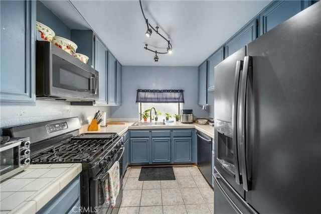 kitchen with light tile patterned floors, tile countertops, appliances with stainless steel finishes, blue cabinetry, and sink