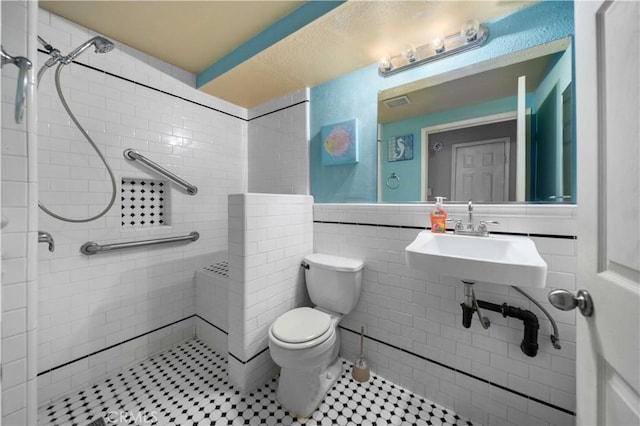 bathroom featuring toilet, tile walls, sink, and tiled shower