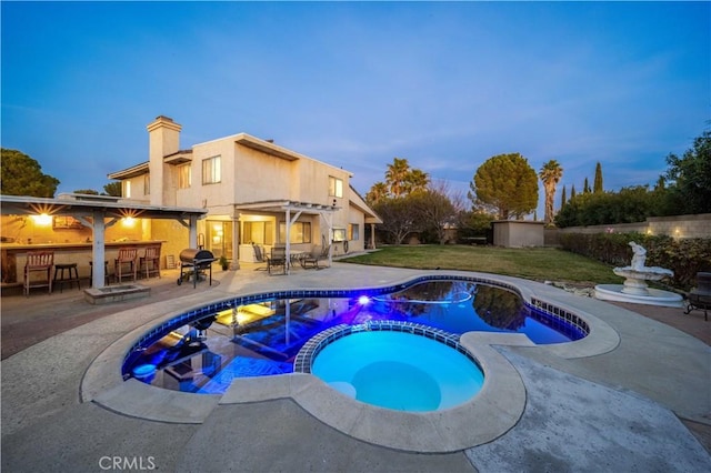 pool at dusk with an outdoor bar, a patio, grilling area, and an in ground hot tub