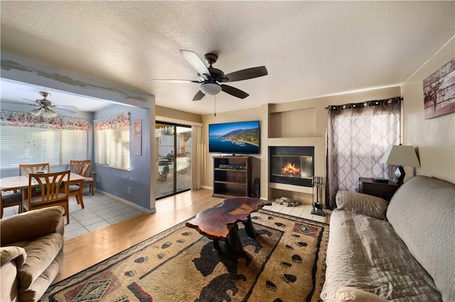 living room with ceiling fan, a textured ceiling, and light hardwood / wood-style flooring