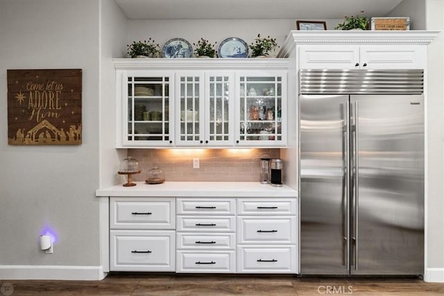 kitchen with decorative backsplash, dark hardwood / wood-style flooring, built in fridge, and white cabinetry