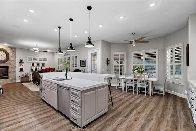 kitchen with ceiling fan, a fireplace, pendant lighting, wood-type flooring, and an island with sink