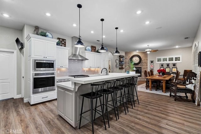 kitchen with a spacious island, hardwood / wood-style flooring, hanging light fixtures, stainless steel appliances, and white cabinets