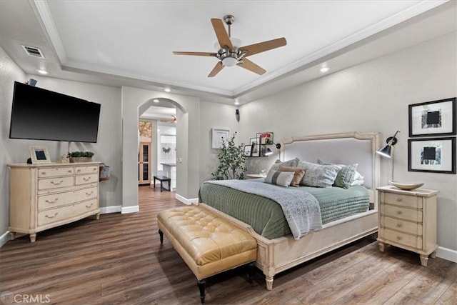 bedroom with ceiling fan, dark hardwood / wood-style floors, crown molding, and a raised ceiling