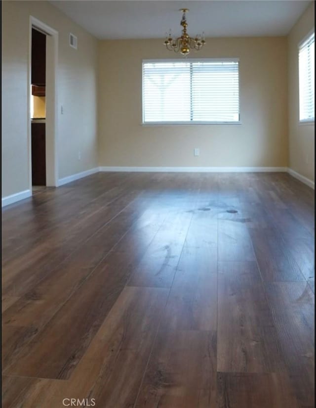 empty room with dark wood-type flooring and a notable chandelier