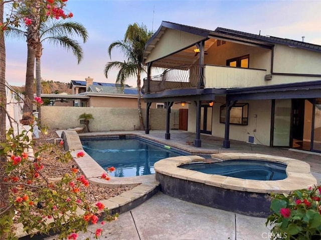 pool at dusk with a patio area and an in ground hot tub