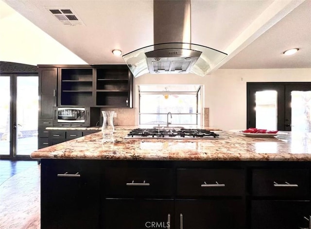 kitchen featuring a wealth of natural light, light stone countertops, island range hood, and french doors