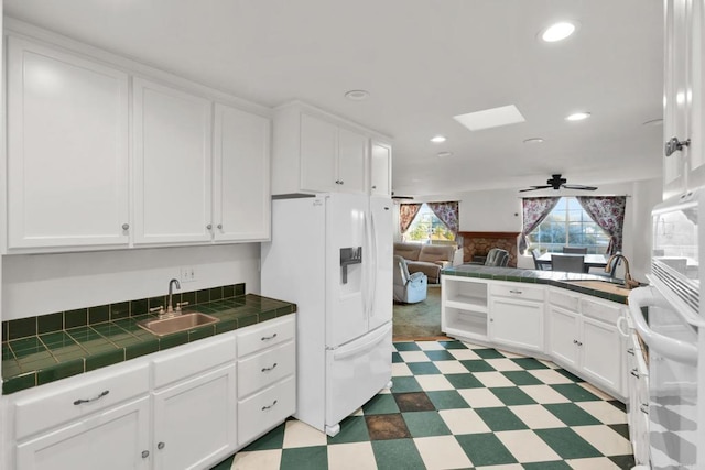 kitchen featuring sink, tile counters, ceiling fan, white refrigerator with ice dispenser, and white cabinets