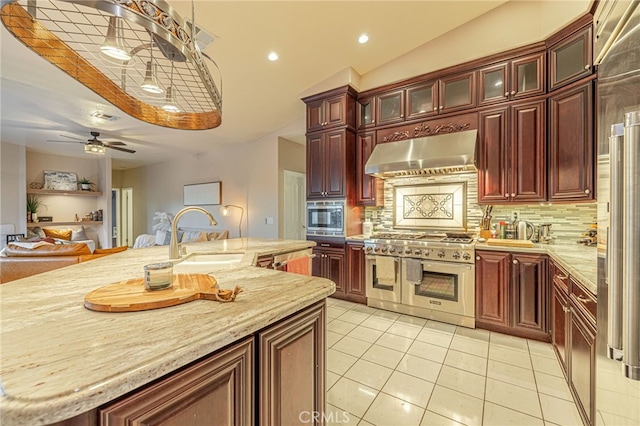 kitchen with sink, appliances with stainless steel finishes, a kitchen island with sink, decorative backsplash, and wall chimney range hood