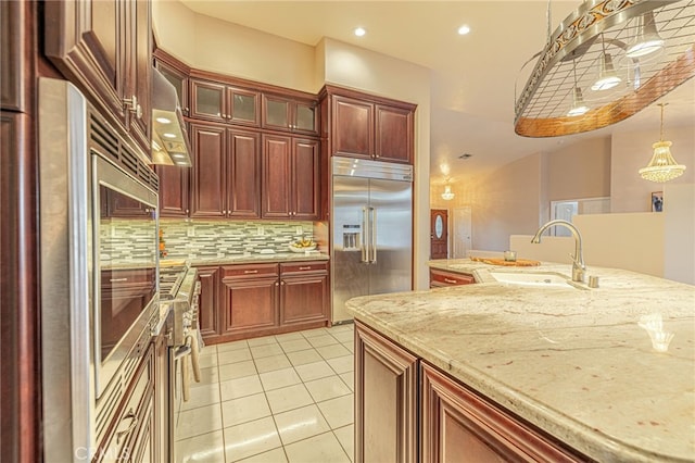 kitchen with light tile patterned flooring, sink, hanging light fixtures, built in fridge, and backsplash