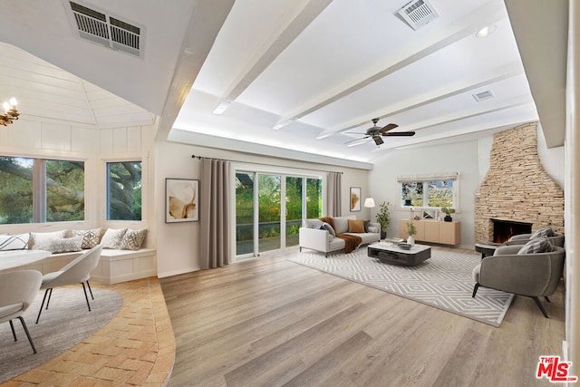 living room with ceiling fan, a fireplace, light hardwood / wood-style flooring, and beamed ceiling