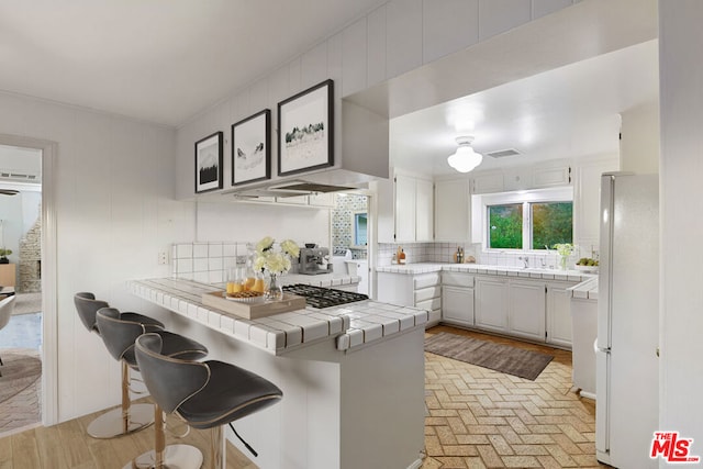 kitchen featuring white cabinets, tile counters, decorative backsplash, kitchen peninsula, and a breakfast bar