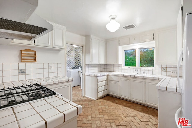 kitchen featuring tile countertops, white fridge, decorative backsplash, white cabinets, and ventilation hood