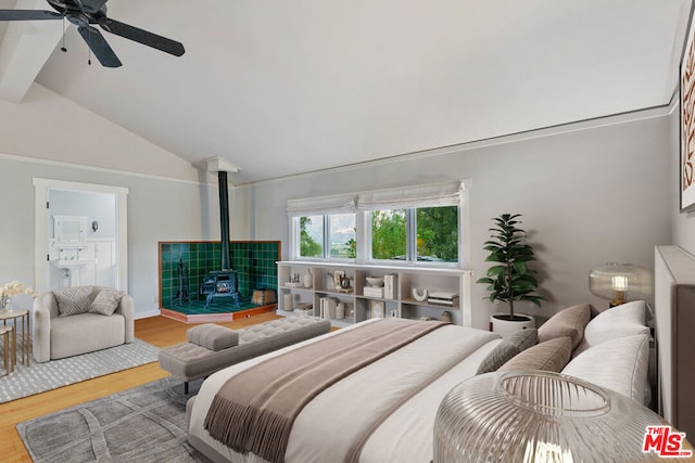 bedroom featuring hardwood / wood-style flooring, a wood stove, ceiling fan, and vaulted ceiling with beams