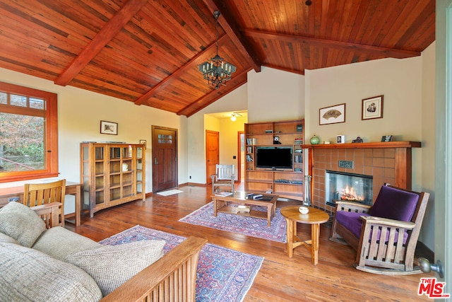 living room with a tiled fireplace, wood-type flooring, beamed ceiling, and a notable chandelier